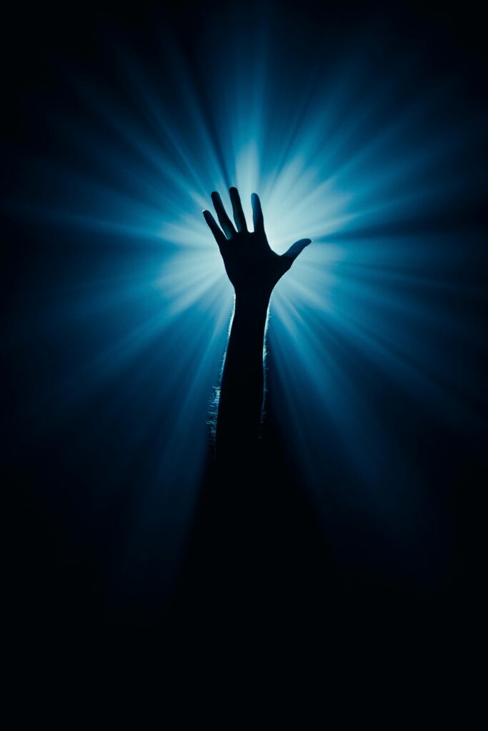 Silhouette of a raised hand against a dramatic blue light background, evoking mystery and inspiration.